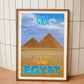 Wood-framed vintage travel poster print featuring the majestic Giza Pyramids in Egypt, embodying the allure and intrigue of emerging travel destinations worldwide